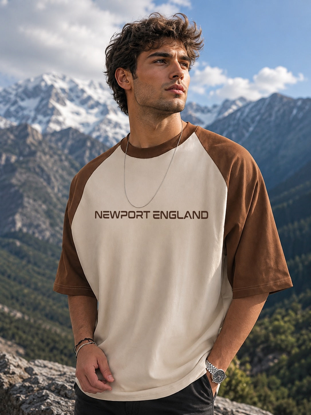 A man wearing a brown and cream raglan t-shirt with 'NEWPORT ENGLAND' printed on the chest, set against a scenic mountain background.